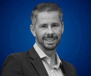 Retrato profesional de José Miguel Sánchez, psicólogo especialista en alto rendimiento, sobre fondo azul.