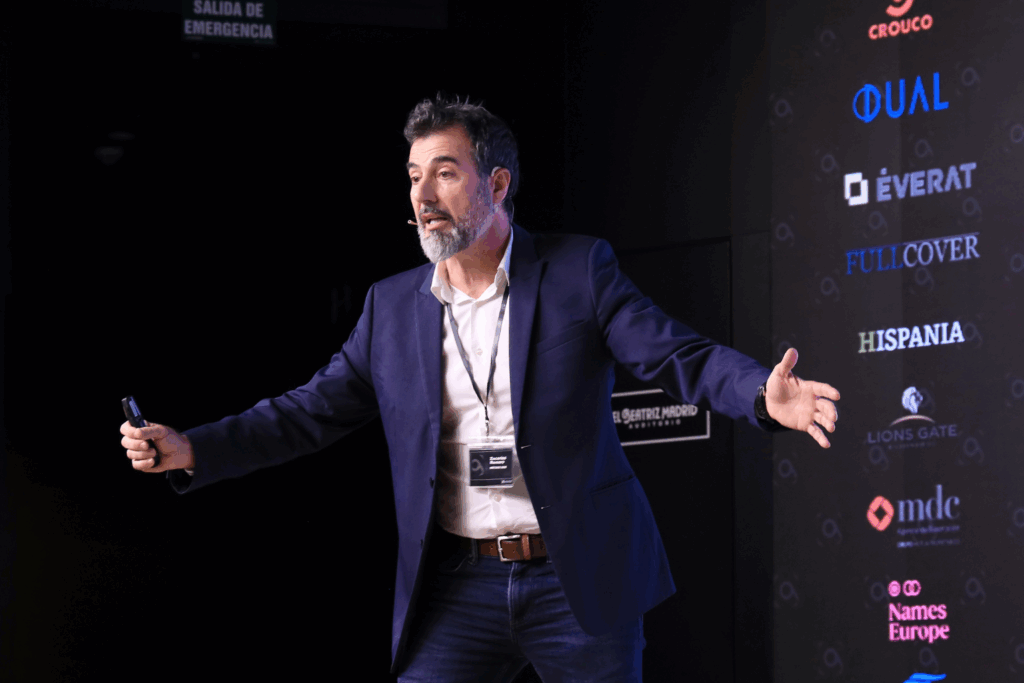 Fotografía de Zacarías Romero ofreciendo una ponencia en el Auditorio Beatriz Madrid, gesticulando con entusiasmo frente a un fondo con logotipos de patrocinadores.