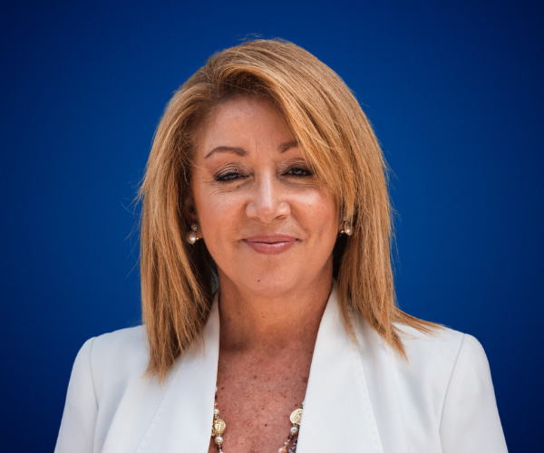 Retrato de Lidia Monzón, conferencista y mentora, con fondo azul.