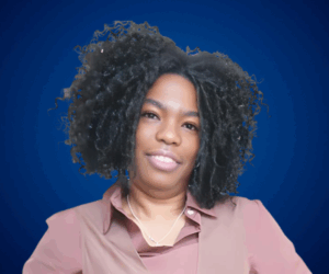 Retrato profesional de Niurys Núñez con blusa en tonos tierra y un fondo azul, proyectando confianza y liderazgo.